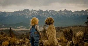 A child and dog sit together facing a vast mountain range, enjoying a serene moment..