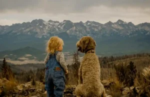 A child and dog sit together facing a vast mountain range, enjoying a serene moment..