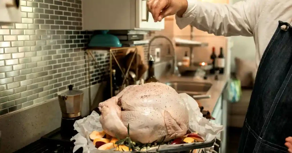 A person seasons an uncooked turkey in a cozy kitchen setting, ready for Thanksgiving dinner..