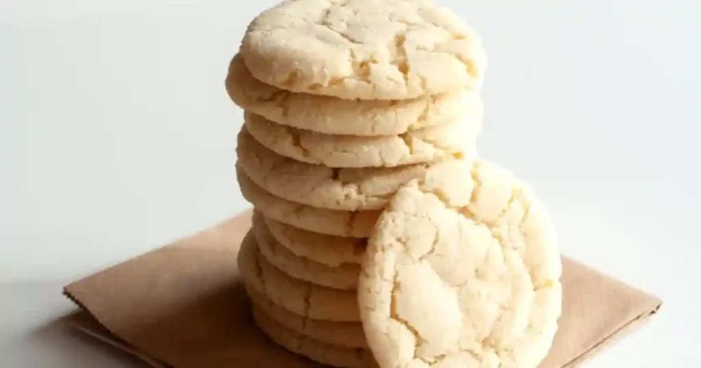 A stack of freshly baked sugar cookies sitting on a brown paper on a white surface, perfect for food blogs..