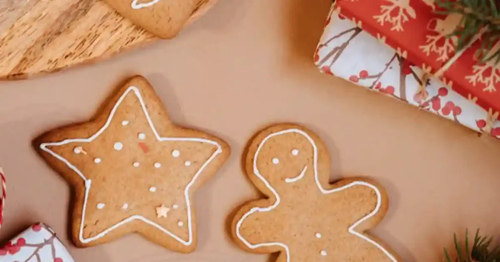 Freshly baked gingerbread cookies with icing, surrounded by holiday gifts and pine leaves..