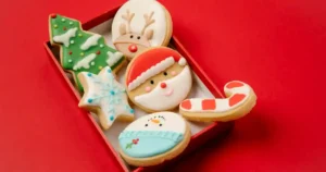High angle of small box with traditional Christmas biscuits covered with colourful icing on red background.
