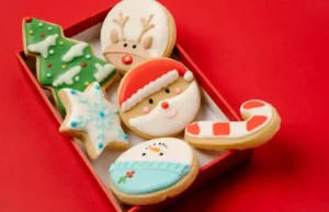 High angle of small box with traditional Christmas biscuits covered with colourful icing on red background.