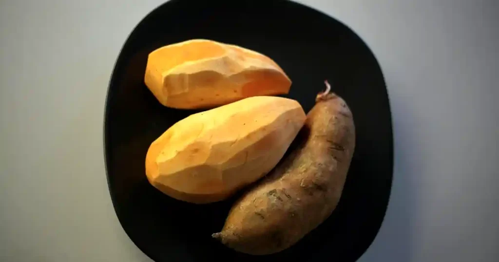 Three sweet potatoes on a black plate, showcasing fresh and rustic appeal..