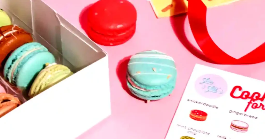 Vibrant assortment of macarons on a pink surface with a festive card and ribbon..