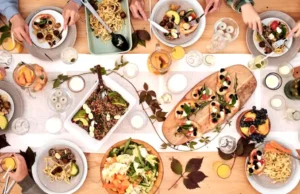 Overhead shot of a vibrant dining table setup with pasta, salads, and decorative candles, capturing a festive gathering..