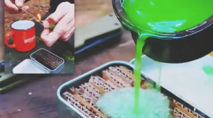 A homemade camping fire starter made from corrugated cardboard soaked in green melted wax and stored in a small metal tin, with one piece being lit outdoors.