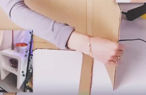 A handmade white nightstand made from cardboard with rounded shelf openings, styled beside a chair with a bowl and candle on top for a modern DIY home decor project.