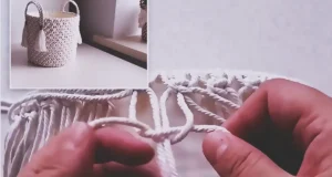 A handmade macrame storage basket made from a recycled plastic bucket, covered with cream rope knots, fabric lining, braided handles, and tassel accents.