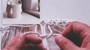 A handmade macrame storage basket made from a recycled plastic bucket, covered with cream rope knots, fabric lining, braided handles, and tassel accents.