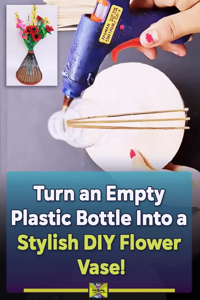 A handmade flower vase made from a recycled plastic bottle, cardboard base, and wooden sticks, painted dark and decorated with red trim while holding colorful handmade flowers.