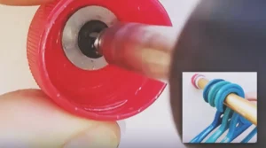 A red plastic bottle cap mounted to a wall and holding a gold wardrobe rail with blue clothes hangers.