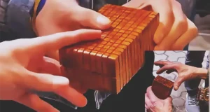 A skilled craftsman demonstrates an intricately carved wooden puzzle box with geometric details, concealed sliding panels, a hidden release mechanism, and a secret interior compartment.