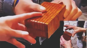 A skilled craftsman demonstrates an intricately carved wooden puzzle box with geometric details, concealed sliding panels, a hidden release mechanism, and a secret interior compartment.