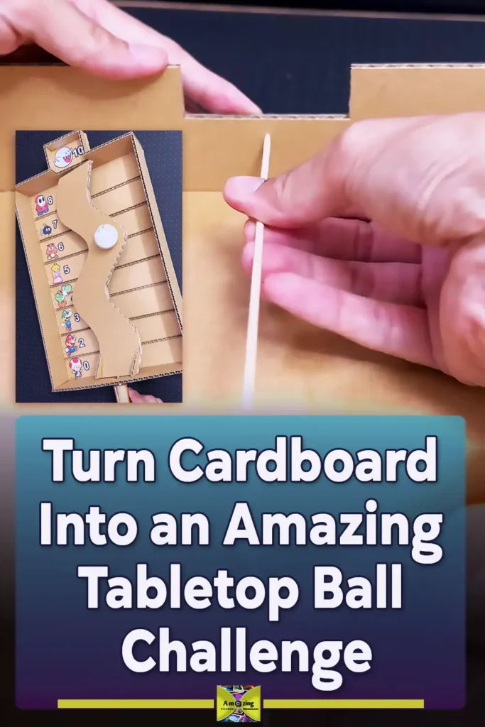 A handmade cardboard balance game with a curved tilting platform, numbered scoring lanes, and a decorated ping pong ball controlled by an external handle made from cardboard and bamboo skewers.