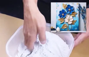 A handmade 3D floral wall art piece on a wood panel, featuring raised drywall putty flowers painted in deep blue and pearl white with metallic gold leaves and turquoise background accents.