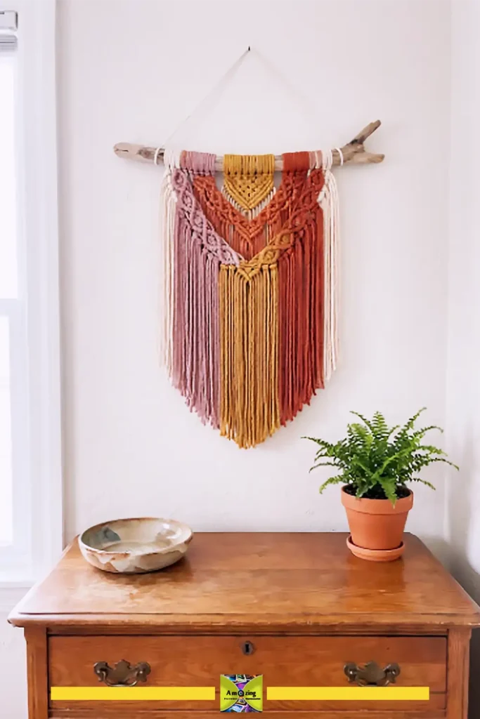 Boho summer yarn wall hanging in sunset colors draped from a natural wooden branch
