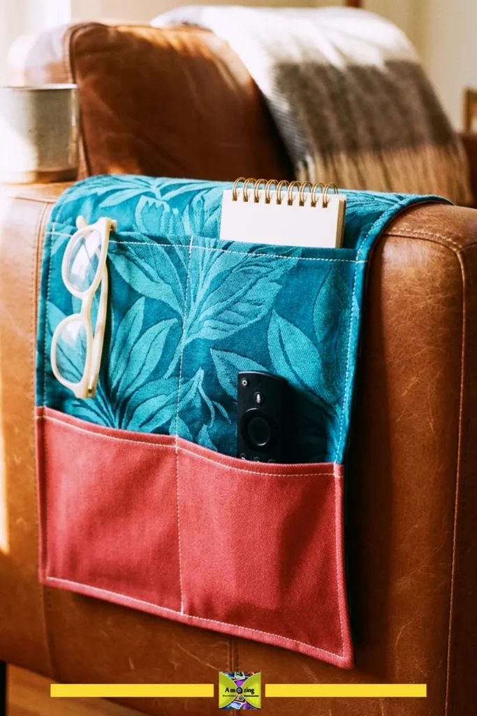 Fabric sofa-arm organizer with glasses, notebook, and remote in its pockets on a leather chair.