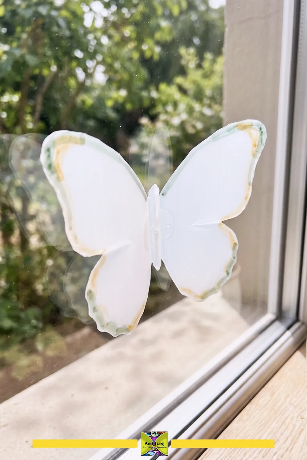 White butterfly window decoration with green and yellow edges attached to a glass window
