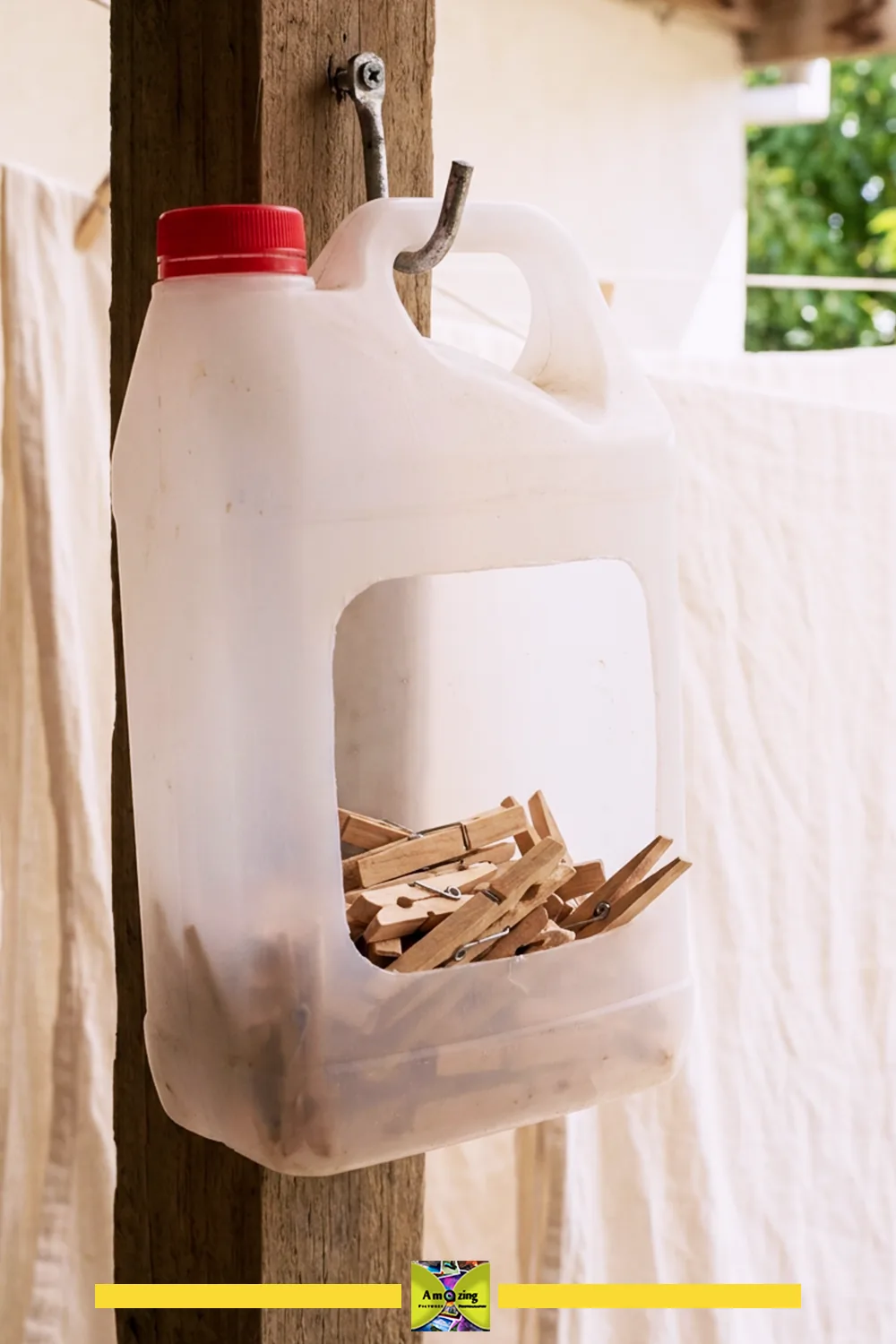 Homemade clothespin dispenser made from a plastic jug hanging on a wooden post
