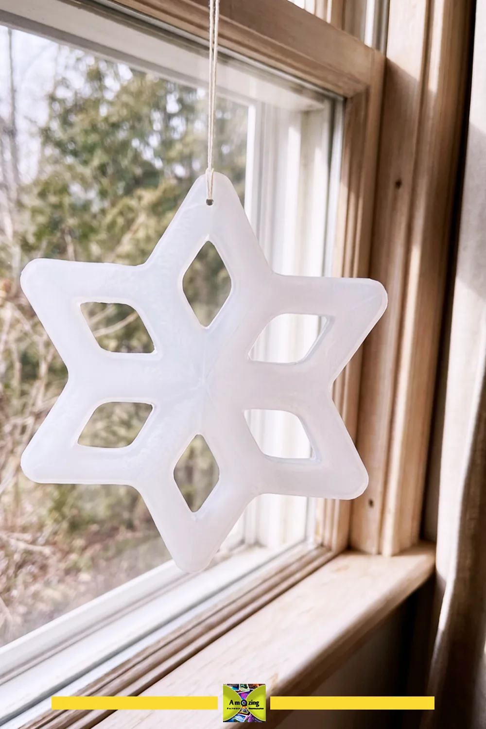 White cutwork snowflake ornament hanging by a string in a sunlit window