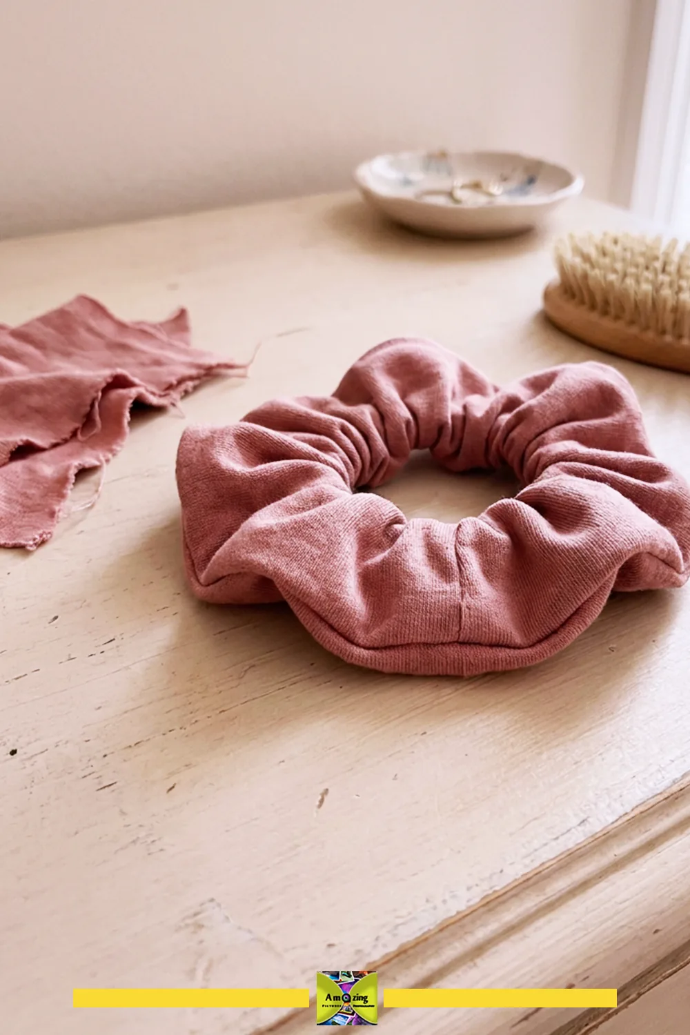 Pink jersey scrunchie on a wooden table with matching fabric and hairbrush nearby.