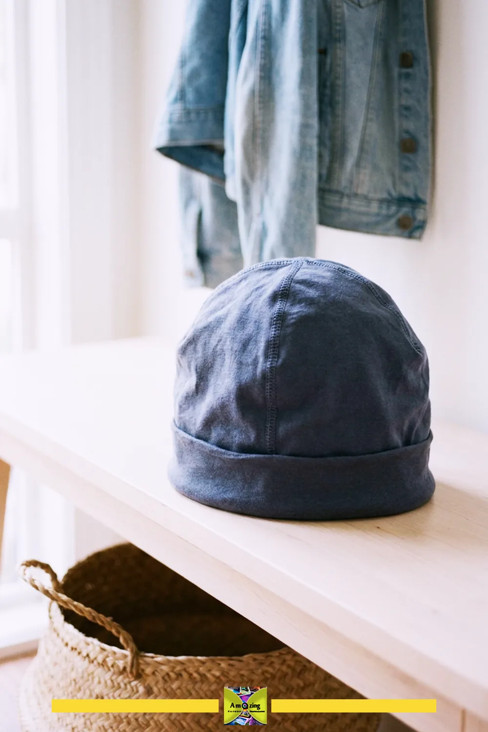 Blue jersey beanie hat on a wooden table with a denim jacket hanging in the background.