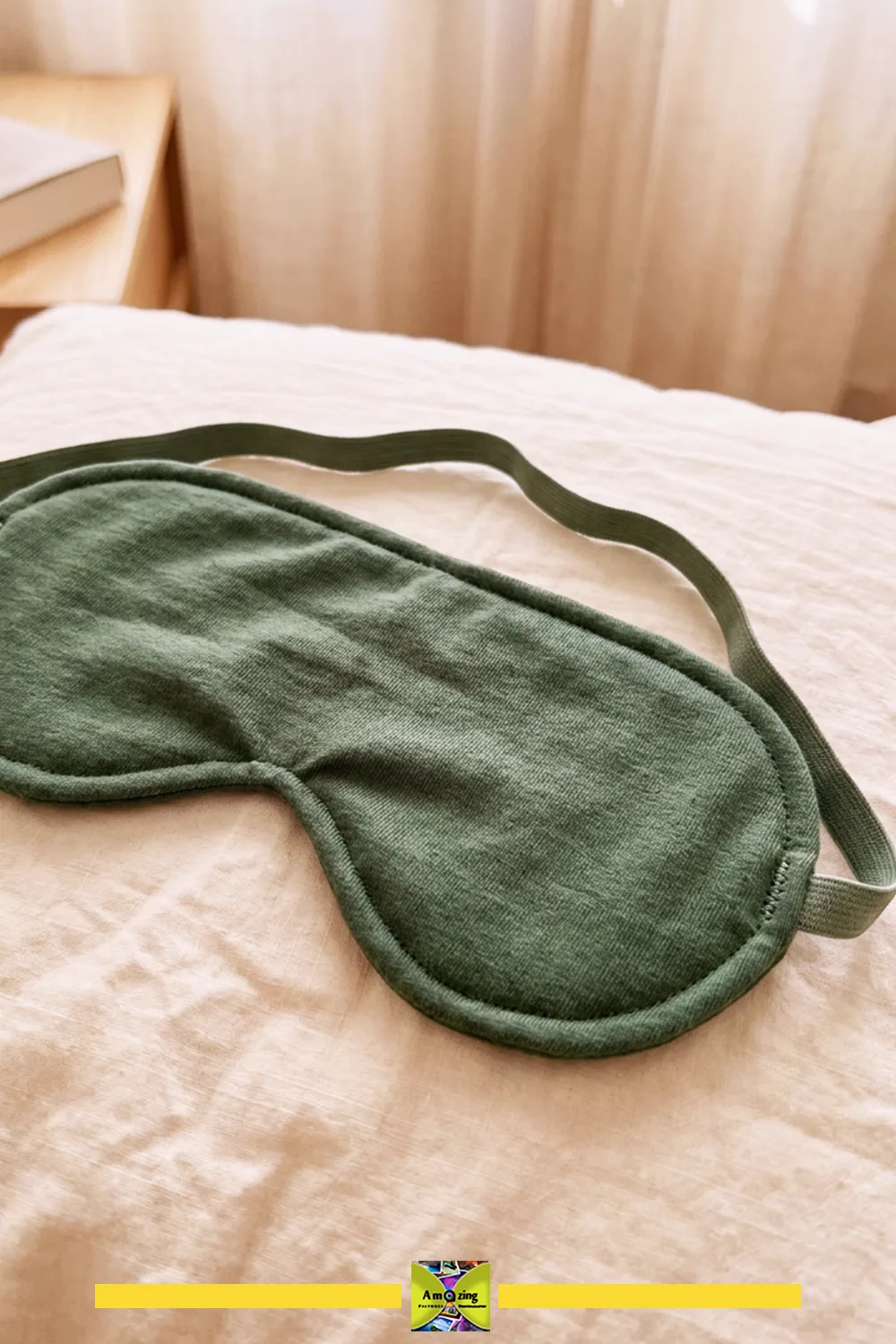 Green jersey fabric sleep mask with elastic band resting on a white bed sheet.