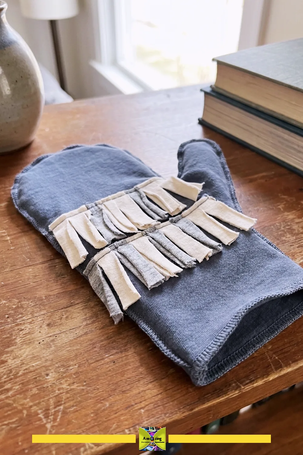 Homemade dusting mitt crafted from repurposed t-shirt fabric with fringe details on a wooden table.