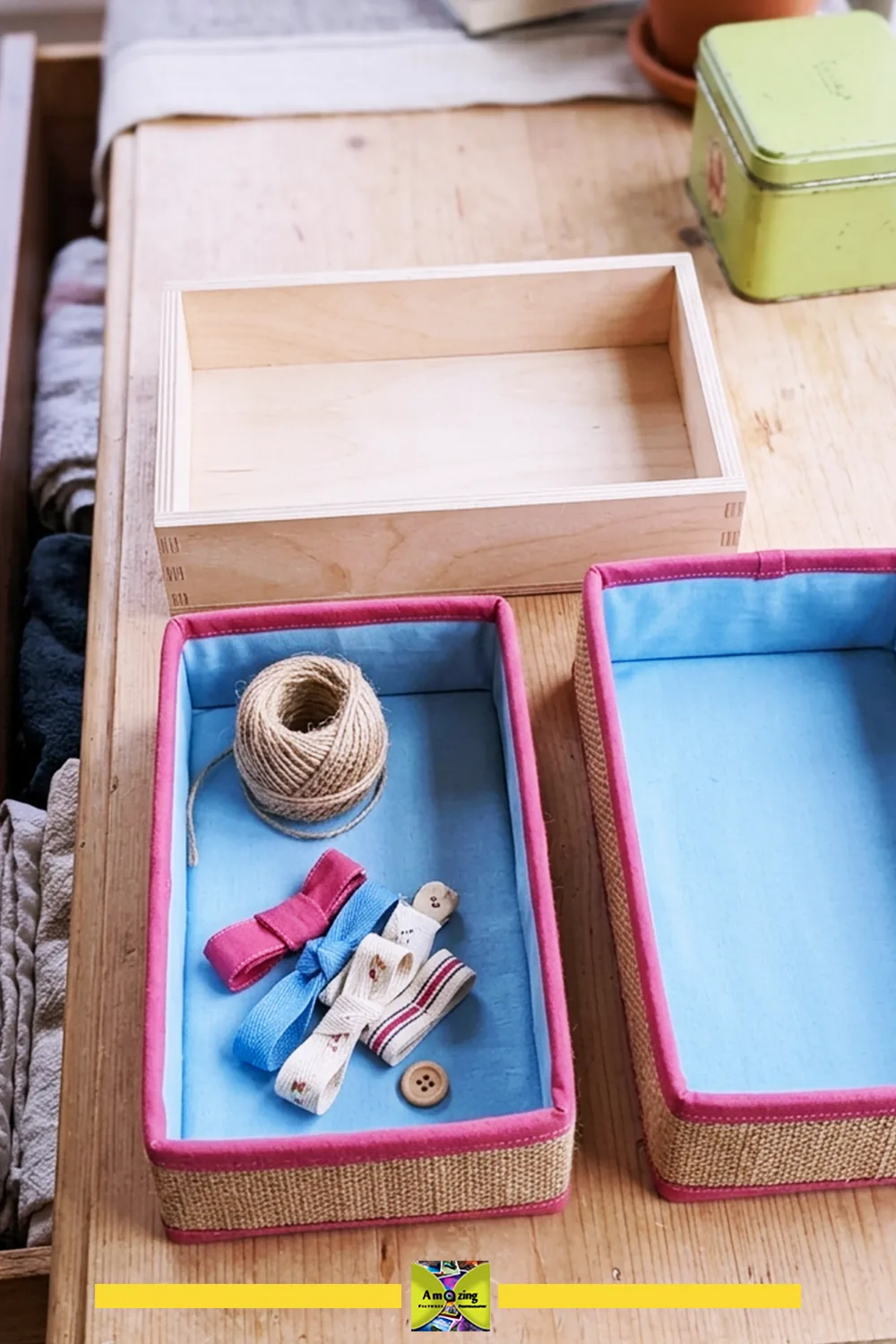 Two fabric-lined drawer bins with pink trim and a plain wooden tray on a wooden table.