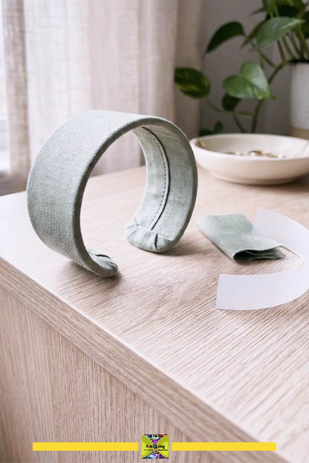A light green fabric-covered open cuff bracelet with matching fabric and plastic insert on a wooden table.