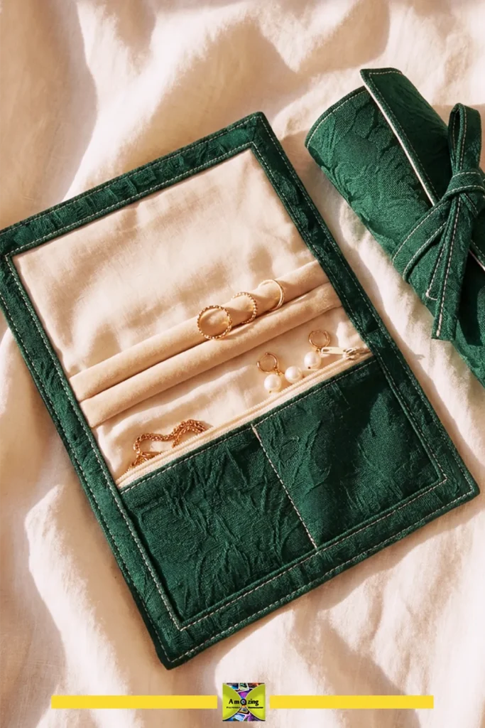 Green fabric jewelry travel roll with smooth lining, holding rings and necklaces on a cream cloth