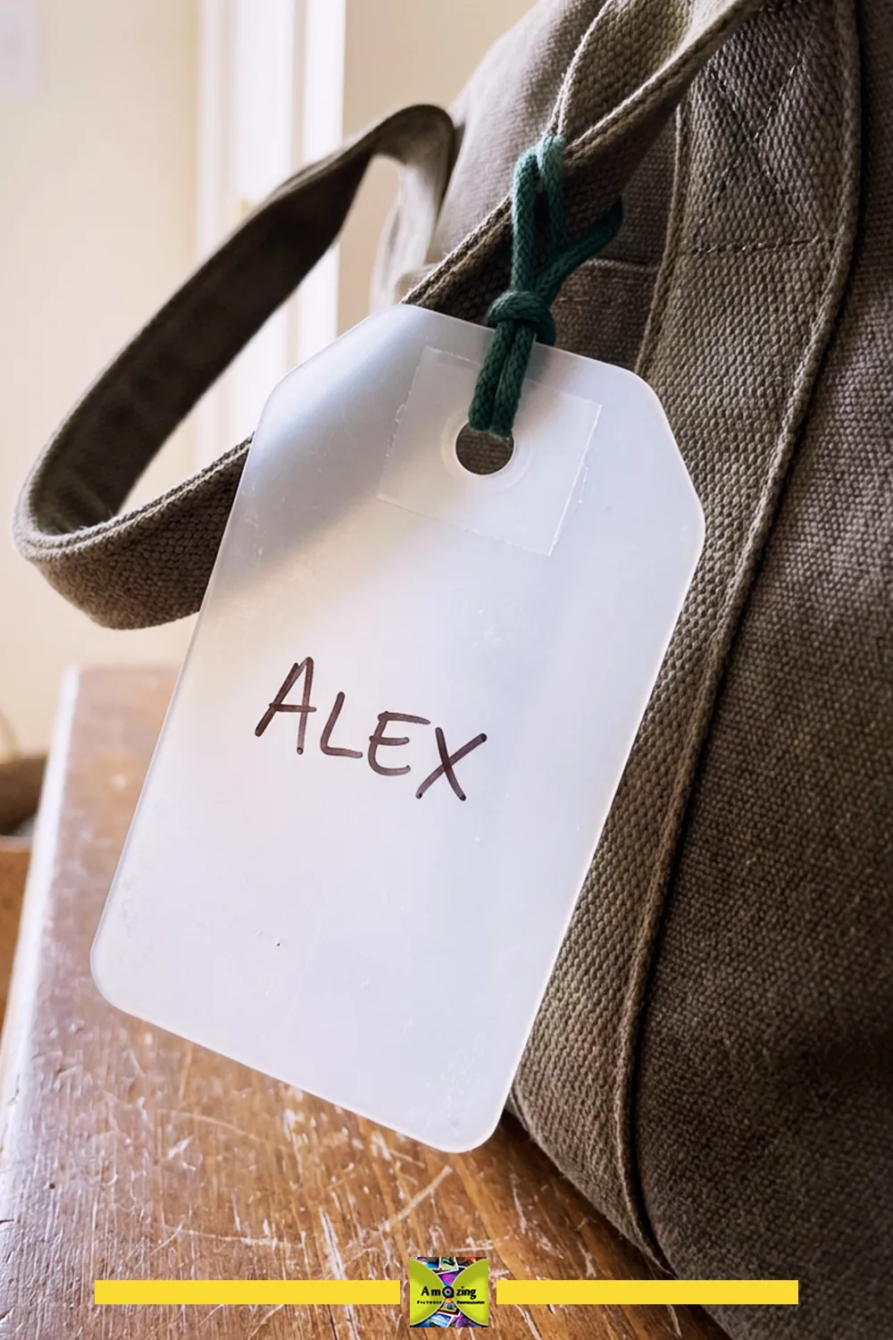 A close-up of a white luggage tag labeled 'Alex' attached to a canvas bag handle.