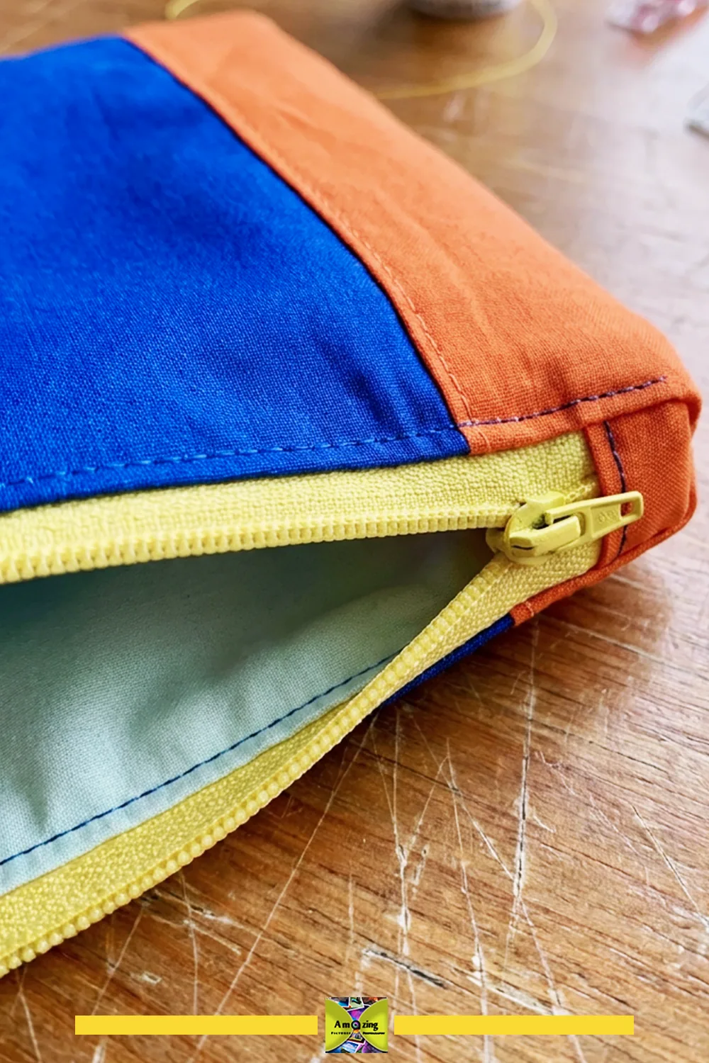 Close-up of a blue and orange fabric pouch with a yellow zipper, partially open on a wooden surface.