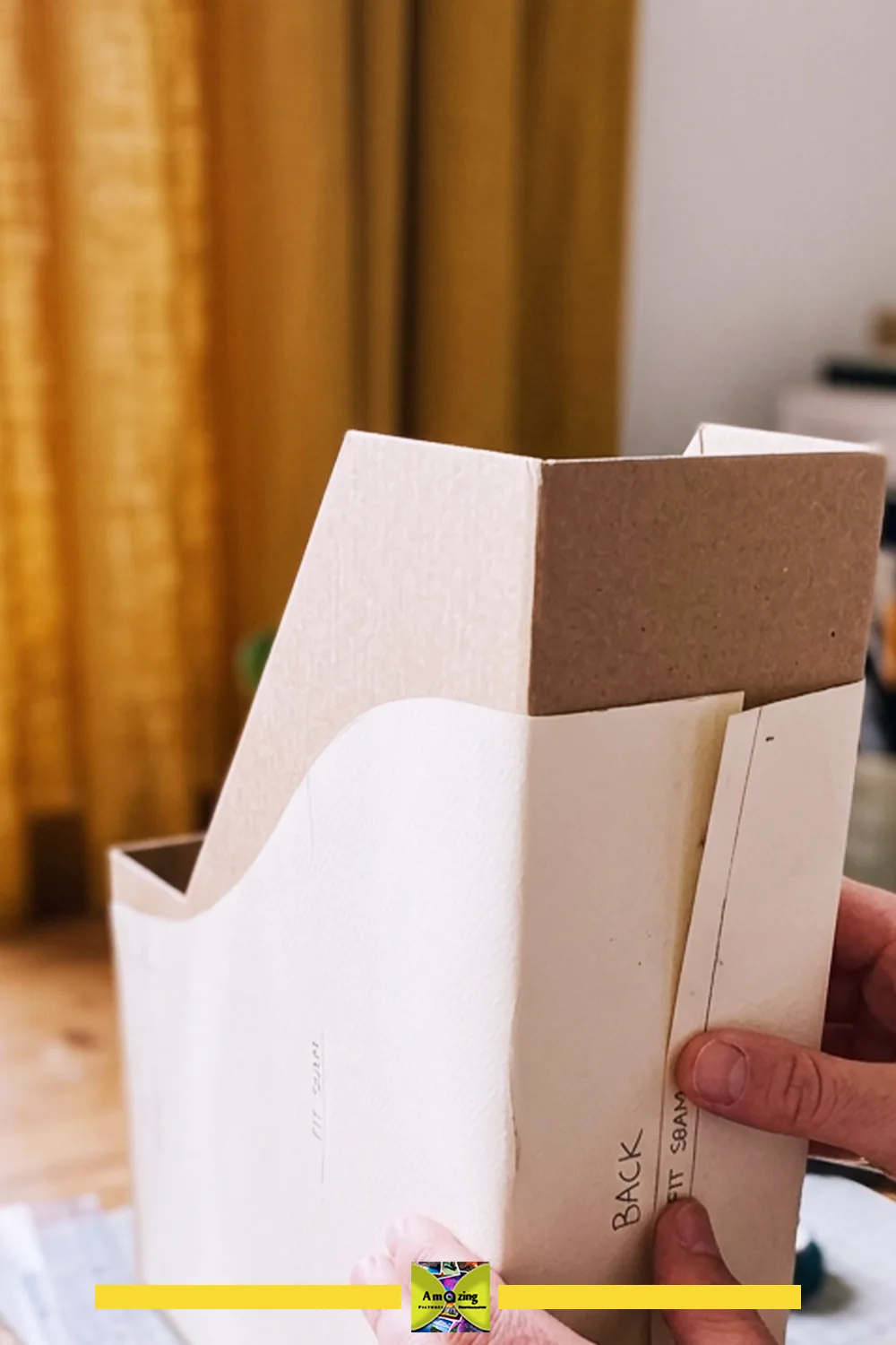 Hands fitting a paper template around a cardboard magazine file holder on a table.