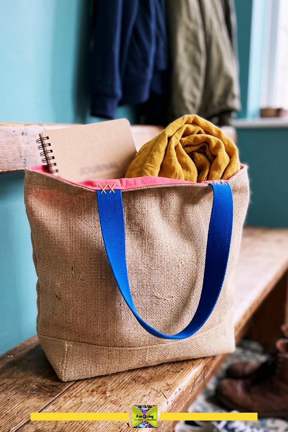 Burlap market tote bag with blue handles, holding a journal and mustard yellow scarf on a bench.