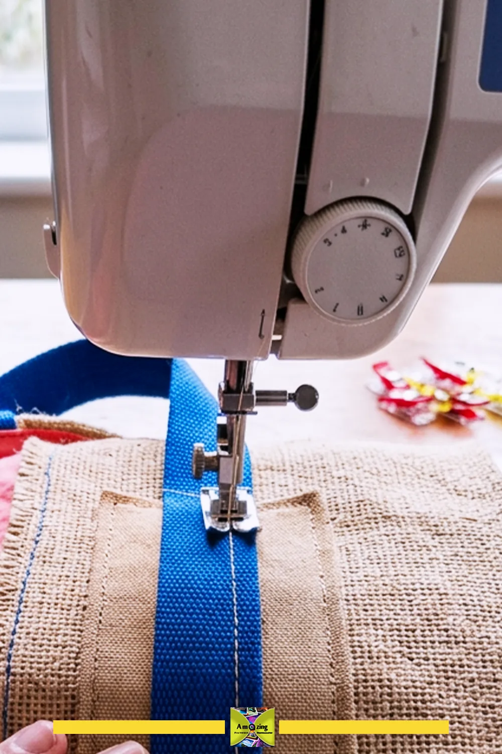 Close-up of a sewing machine stitching a blue handle onto a burlap market tote bag.