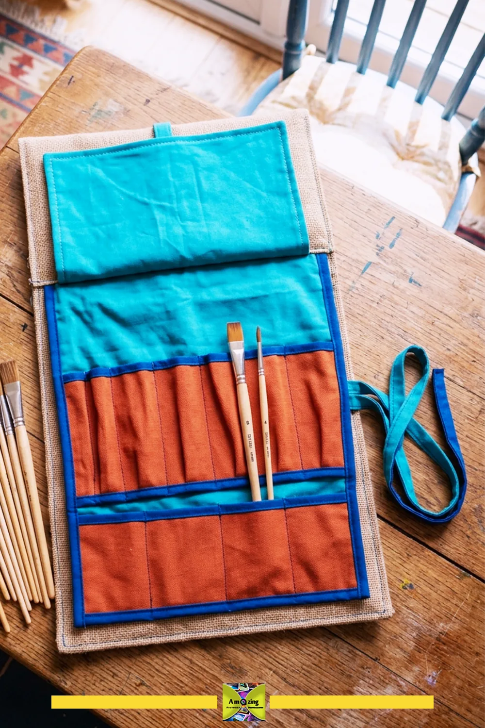 Open fabric paintbrush roll organizer with brushes beside it on a wooden table