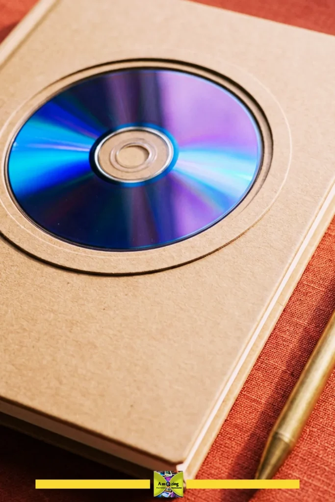 Close-up of a refillable notebook cover with a CD in a cardboard sleeve and a gold pen beside it.