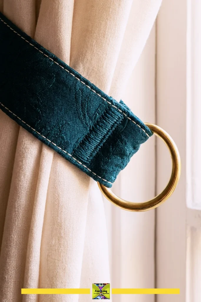 Close-up of a cream curtain secured with a teal fabric tieback and brass ring