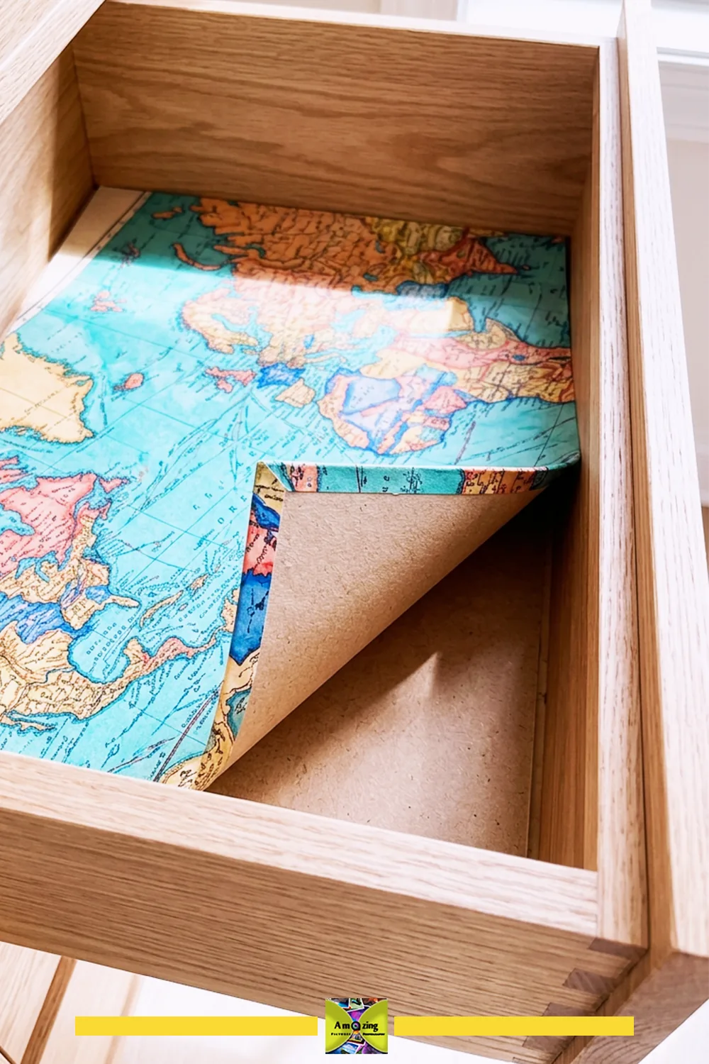 Map-covered liner panel partly lifted inside an open wooden drawer.