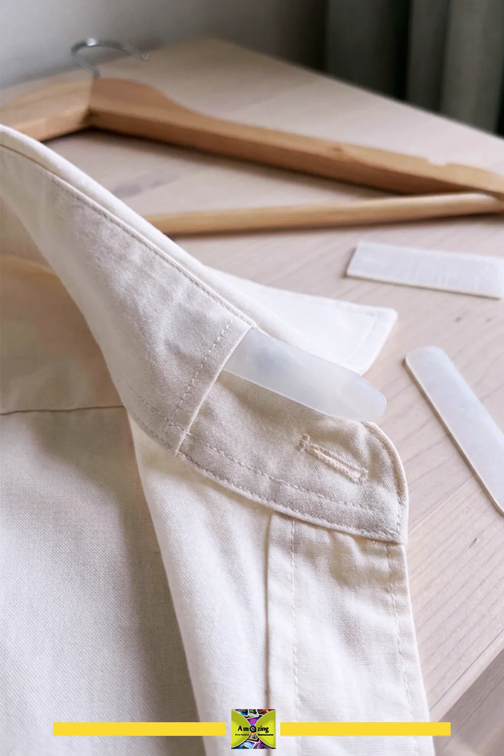 Close-up of a shirt collar with a plastic collar stay inserted, wooden hangers and extra stays nearby.