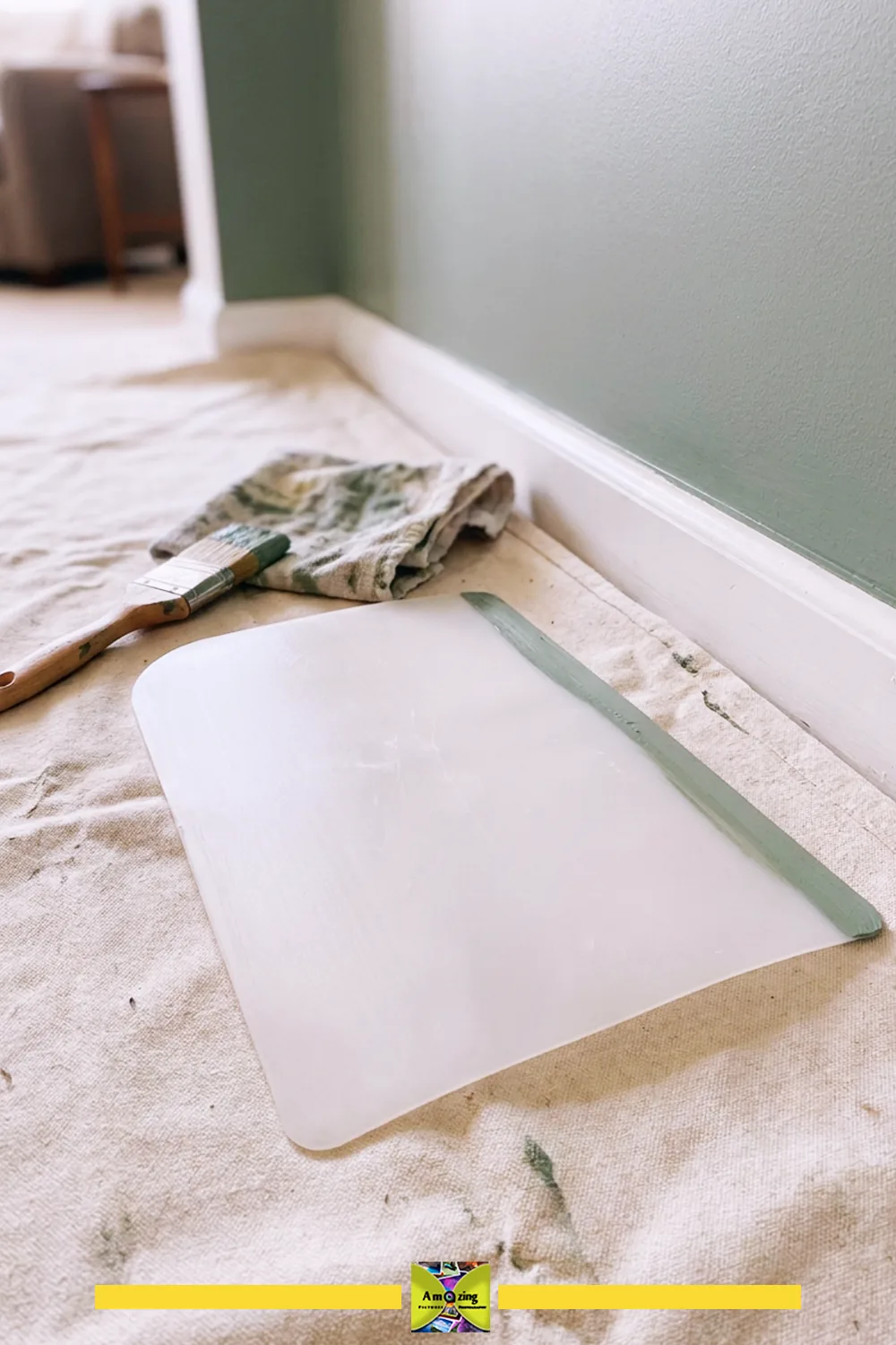 Paint edge shield, brush, and cloth on a drop cloth near a freshly painted wall and trim.