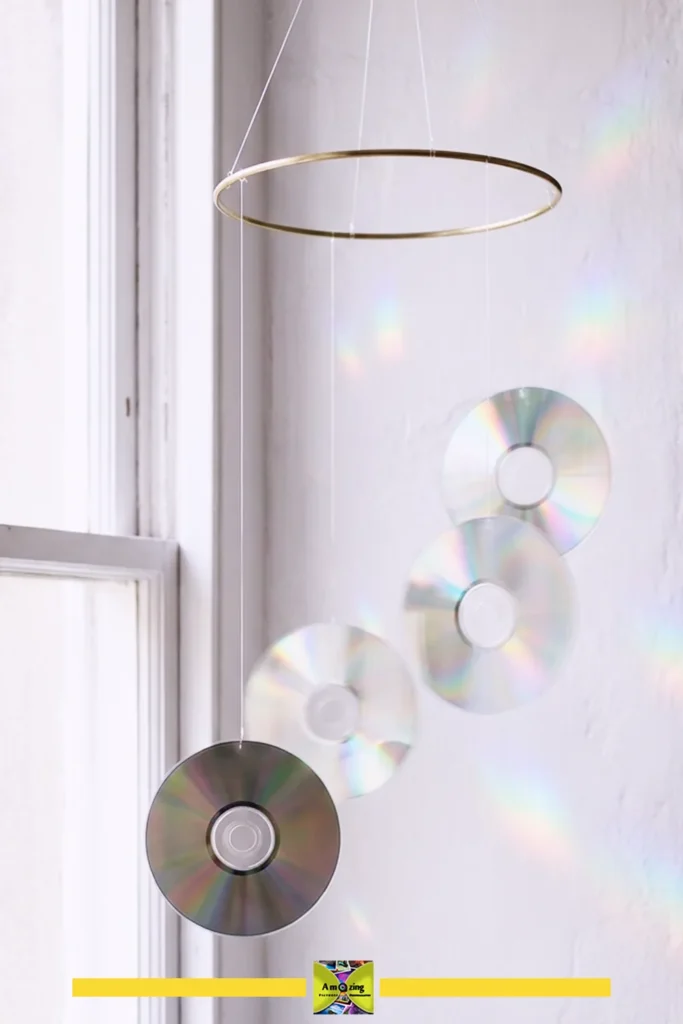 Hanging mobile made of CDs suspended by strings near a window, reflecting rainbow light patterns.