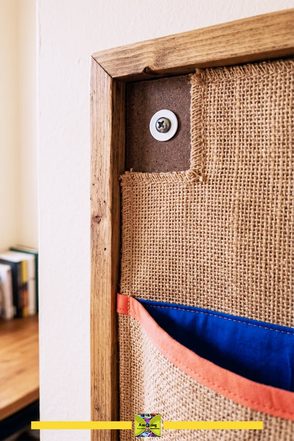 Close-up of a wall pocket organizer with burlap fabric, blue pocket, and screw mounting through the backing.