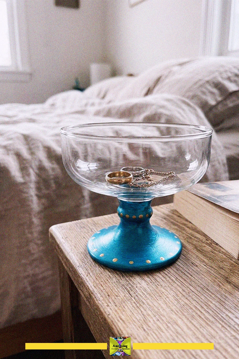 Footed glass dessert cup with a painted blue base used as a jewelry holder on a bedside table