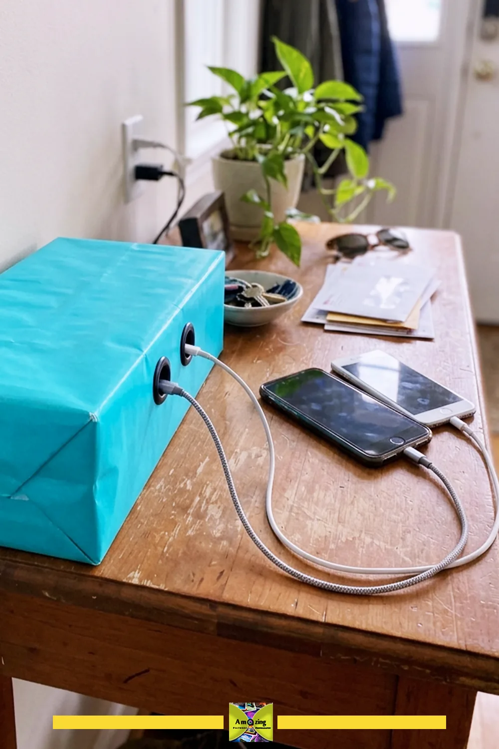DIY cardboard cable organizer wrapped in blue paper, holding charging cables and phones on a wooden table