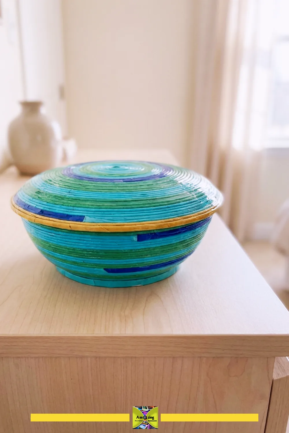 Handmade coiled bowl with a lid, crafted from colorful recycled magazine paper, on a wooden surface.
