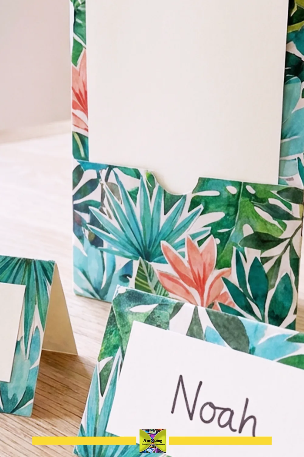 Handmade place cards and menu holders with vibrant tropical magazine cutout designs on a wooden table.