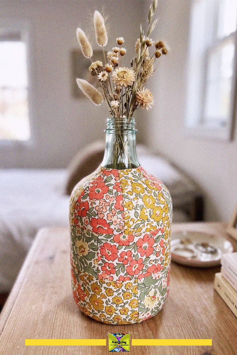 Upcycled glass bottle vase covered in floral fabric decoupage, holding dried flowers on a wooden table